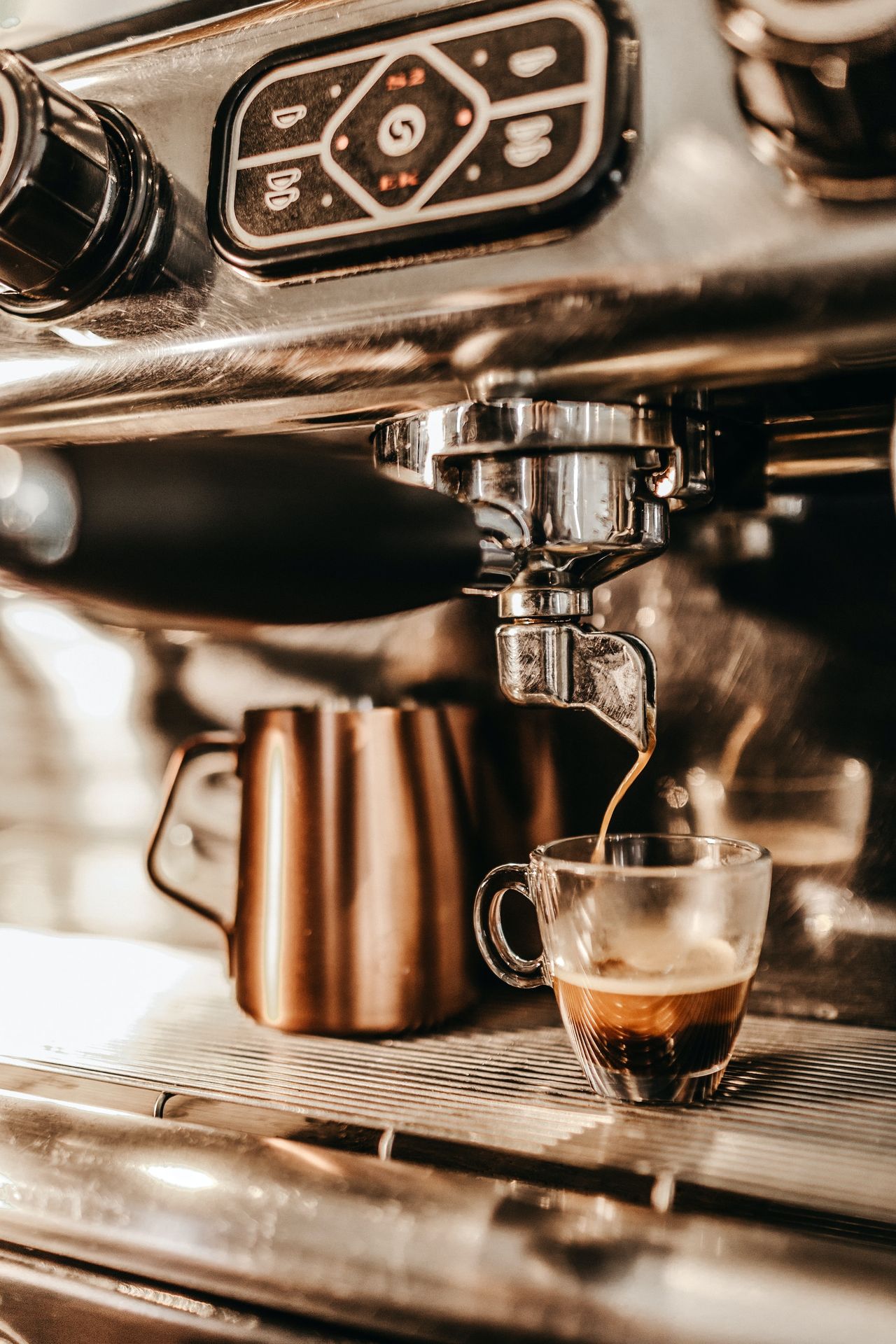 grey industrial coffee maker pouring espresso in clear glass cup